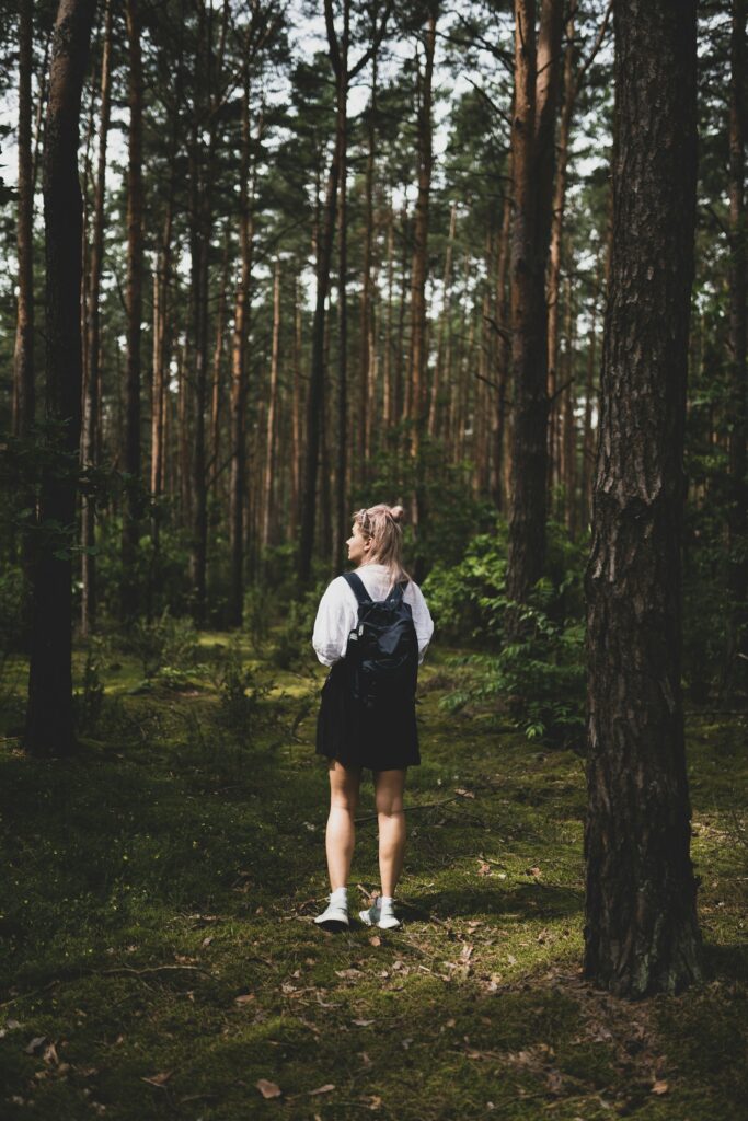 Zdjęcie przedstawiające dziewczynę z plecakiem w lesie 